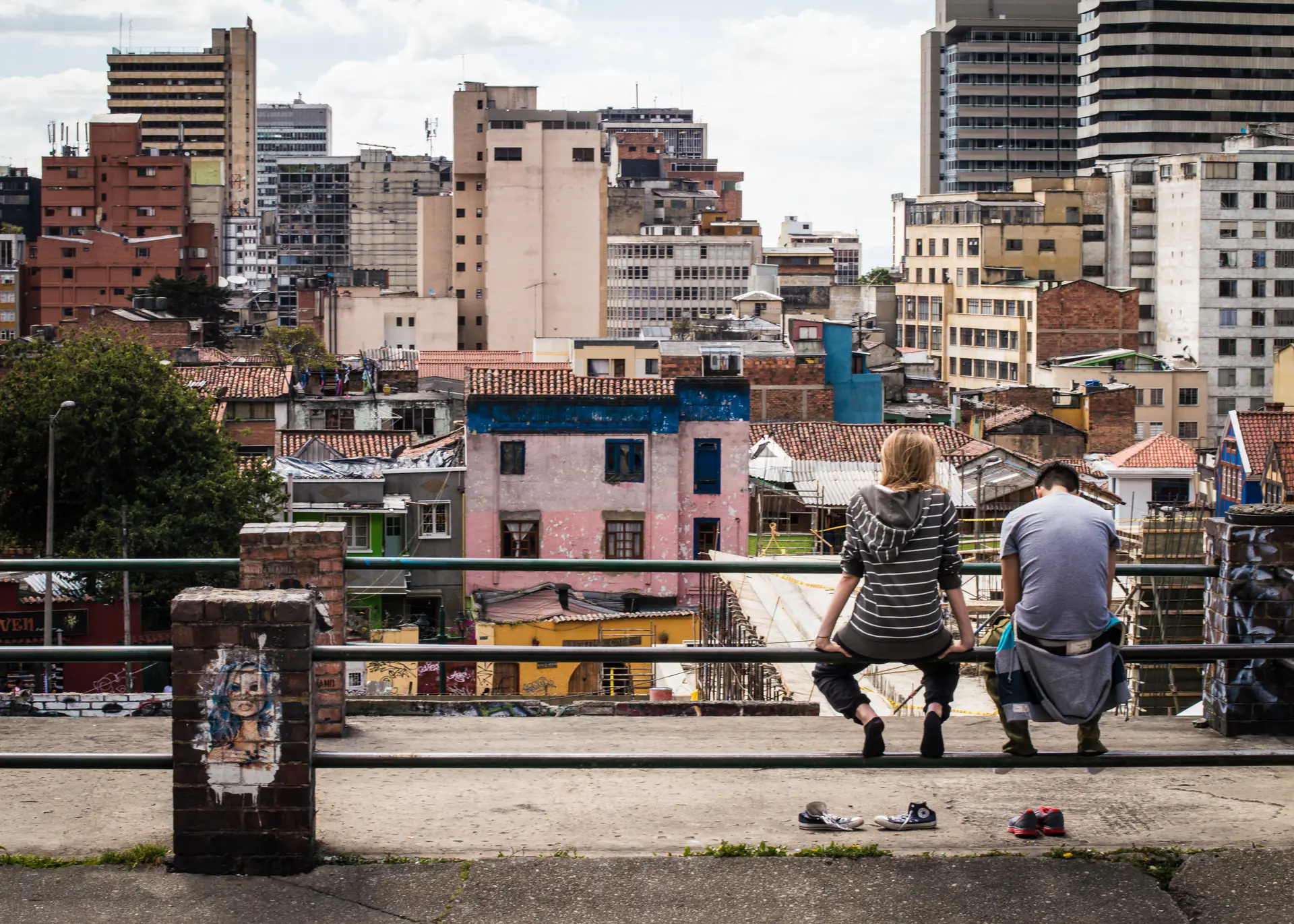 Two people sitting on a railing overlooking a dense city.
