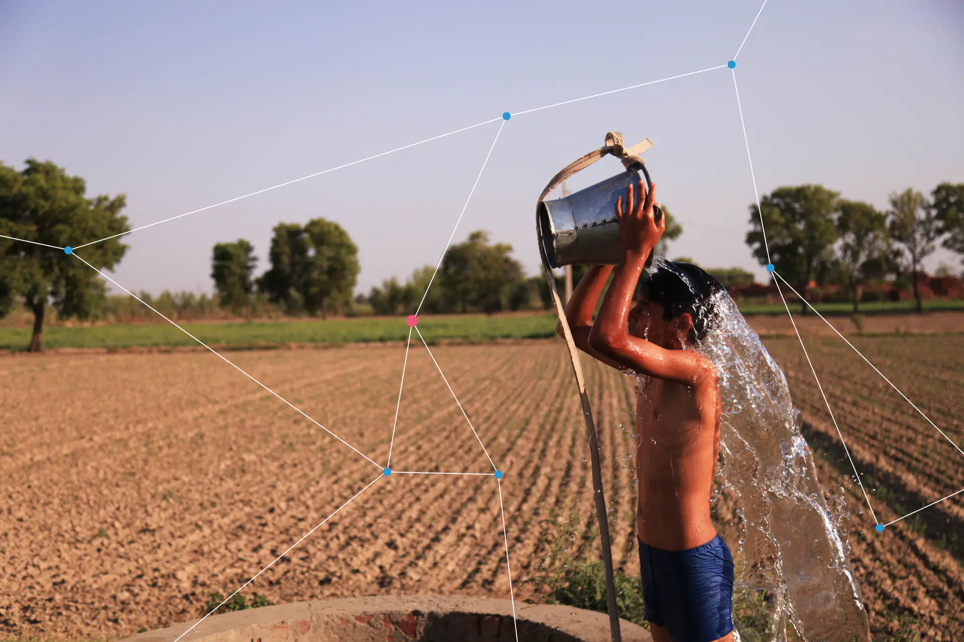 A boy pouring a bucket of water over himself beside a dry field.